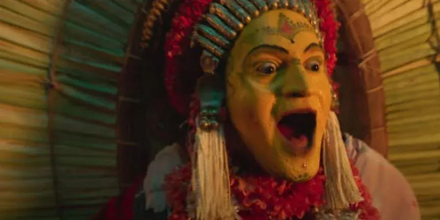 A man in ornate garb and garish yellow makeup takes on the persona of an angry demigod