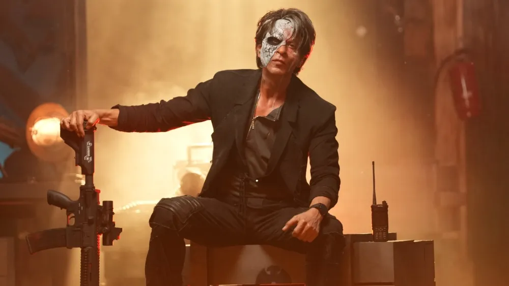 Shah Rukh Khan in the movie Jawan poses dramatically with an assault rifle.