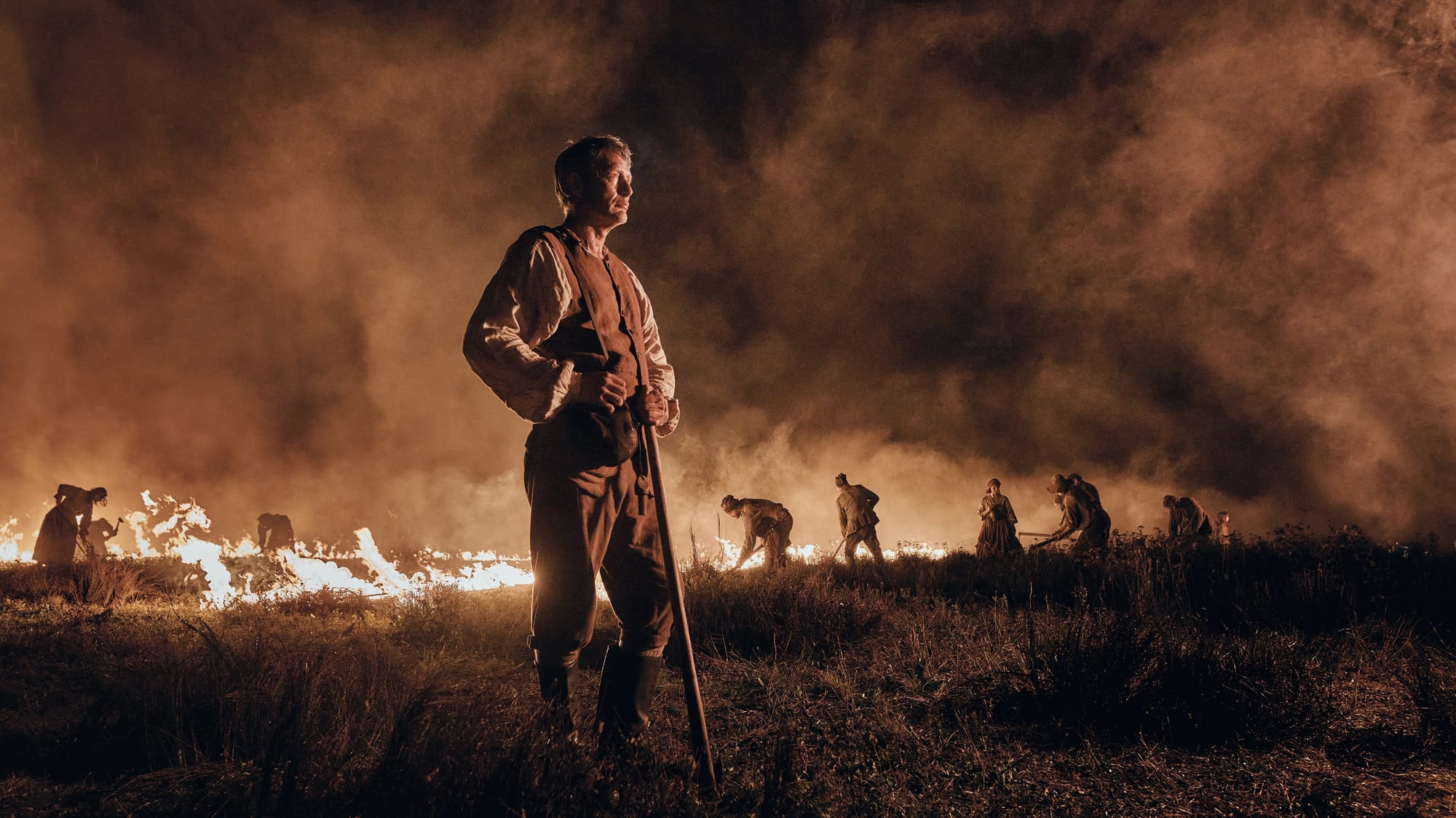 Workers control the flames of a fire across a stretch of land at night